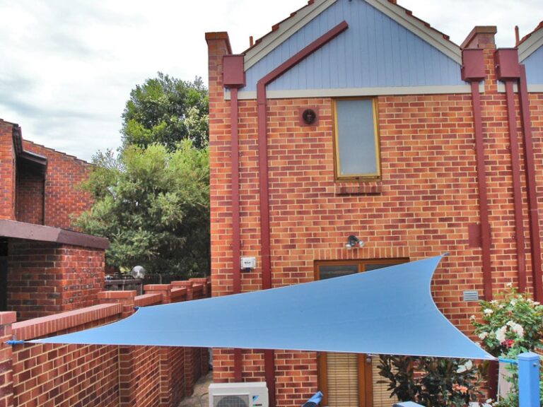 Blue-grey shade sail beside a brick home