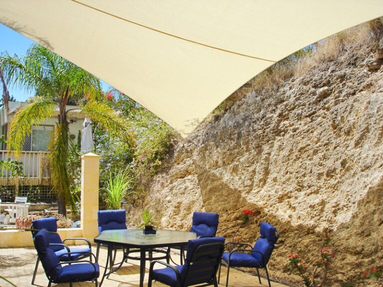 Cream shade sail over a patio beside a limestone wall