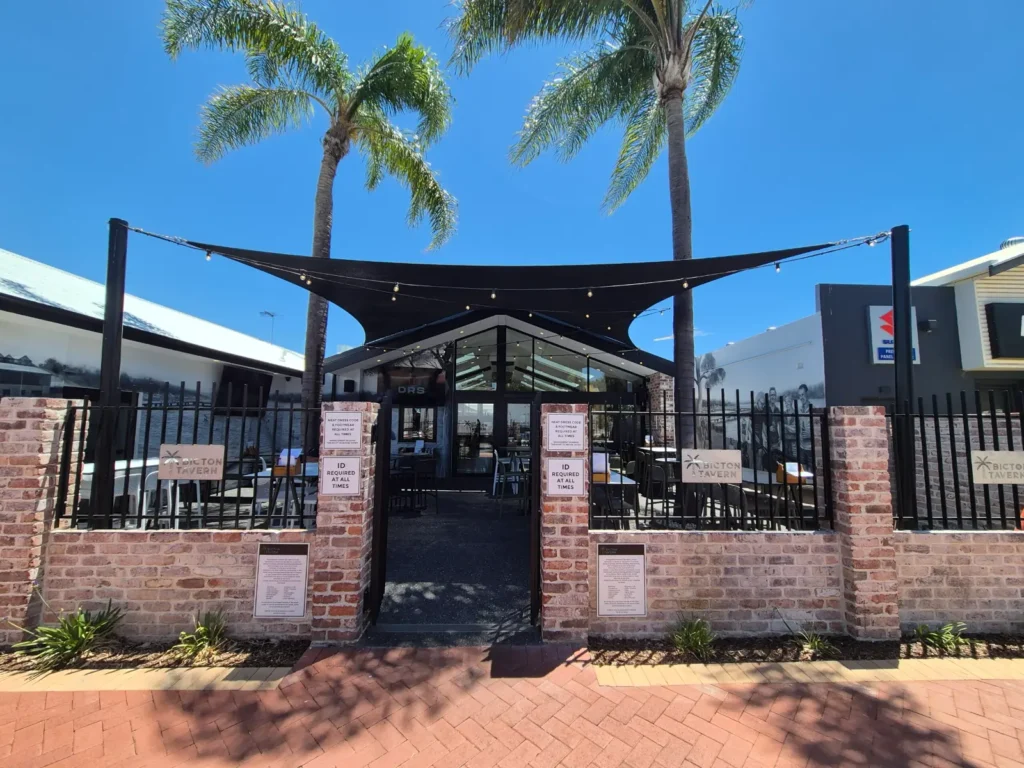 Black shade sails over a courtyard entrance with palm trees