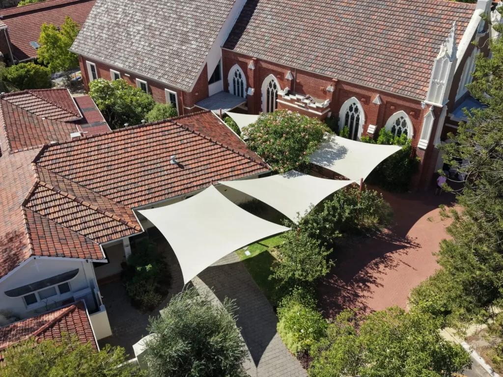 White shade sails over a courtyard beside a brick church in Perth